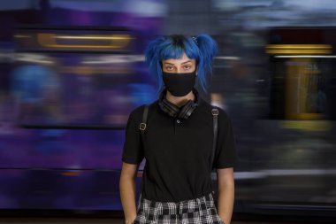 Tıbbi maske takmış, metro geçmişi bulanık genç bir kız tren istasyonunda bekliyor.