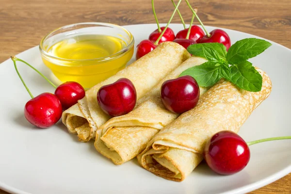 Homemade dessert. Fried pancakes with honey. Crepe with black cherry on white plate background. — Stock Photo, Image