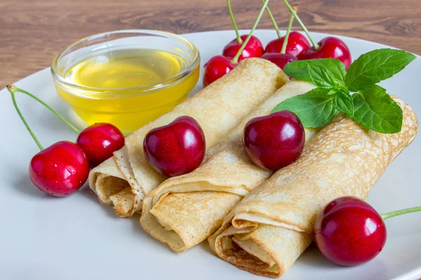 Homemade dessert. Fried pancakes with honey. Crepe with cherry on white plate background. — Stock Photo, Image