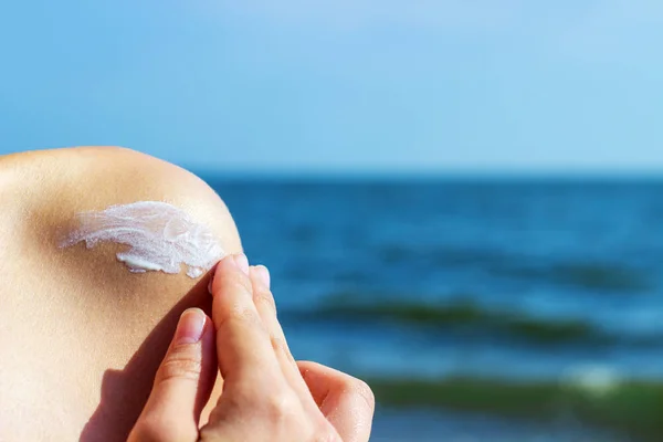 Woman applying sunscreen at the beach on hot summer day. A girl smears a shoulder with sunscreen — Stock Photo, Image