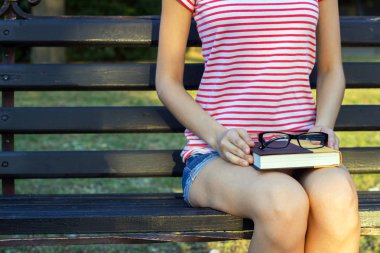 Kız parkta bir kitap ile bir tezgah ve kucağında siyah gözlük. Bir öğrenci parkta bir kitap okuma