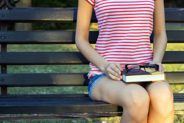 Kız parkta bir kitap ile bir tezgah ve kucağında siyah gözlük. Bir öğrenci parkta bir kitap okuma