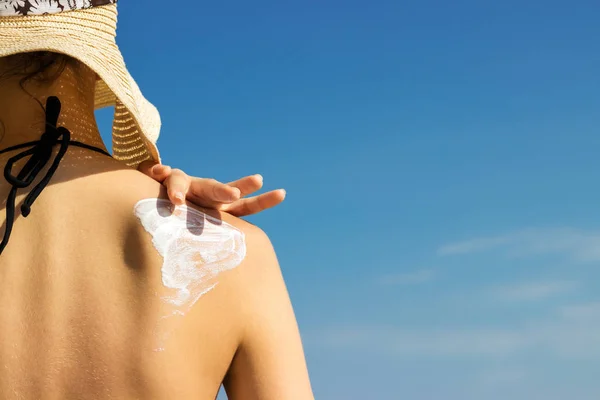 Woman in a hat applying sunscreen on her shoulder — Stock Photo, Image