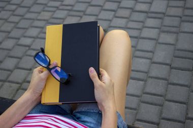 Kız parkta bir kitap ile bir tezgah ve gözlük kucağında. Bir öğrenci parkta bir kitap okuma