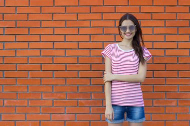 Çizgili tişört ve kot şort giyen güzel kadın. Kırmızı tuğla duvar arka plan. Boş alan