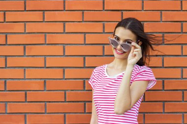 Sevimli kız bir kenara kırmızı tuğla duvar arka plan üzerinde seyir pembe moda gözlük takan portresi kapatın. Metin tasarım için boş alan.