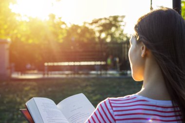 Açık havada'nde Günbatımı bir kitap okuma bir bankta oturan çekici kadın. Arkadan Görünüm