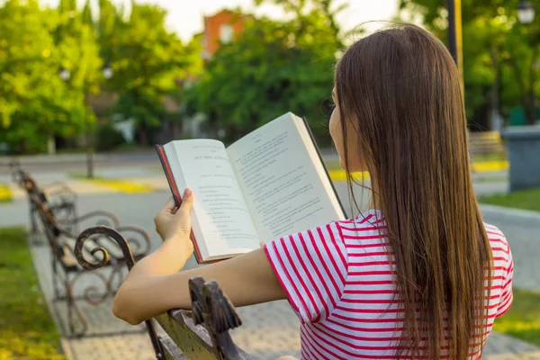 Kırmızı ve Beyaz tişört parkta bankta bir kitap yaz günde zevk çekici kadın. Güzel kız rahatlatır ve parkta bankta bir kitap okur.