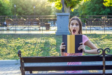 Kız parkta bir kitapla şaşırmış ve şok. İnsani duygular yüz ifadesi.