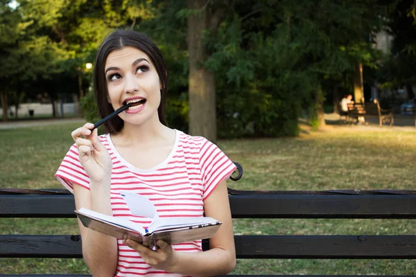 Çekici kız bir kitap ve bir kalem parkta onun ağzına düşünüyorum. İnsan duyguları