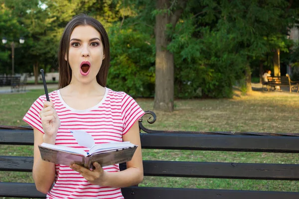 Bir fikir olan ve yeşil park arka plan üzerinde poz bir kalem tutan genç güzel kız.