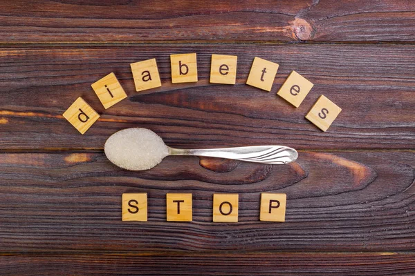 Diabetes STOP block wooden letters and sugar pile on a spoon. Concept Diabetes Prevention