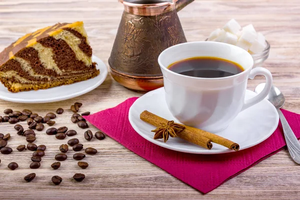 Eine Tasse schwarzen Kaffee auf Untertasse mit leckerem Kuchen. weiße Zuckerwürfel in einer Schüssel, Teelöffel, Anis, Zimtstangen und anderes Zubehör für den Kaffee auf dunklem Holzgrund. — Stockfoto