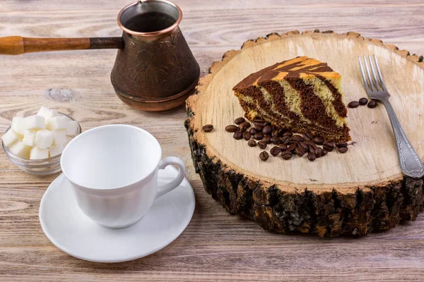 Un pastel de chocolate sobre un tocón de madera con una taza de café, tenedor, granos de café y un tazón con terrones de azúcar sobre un fondo de madera brillante — Foto de Stock