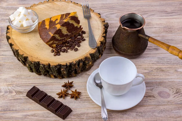 在木树桩上的一块巧克力蛋糕的顶部可以看到, 上面有咖啡杯、茶匙、叉子、子、咖啡豆、巧克力棒和在明亮的木制背景上盛放糖块的碗 — 图库照片