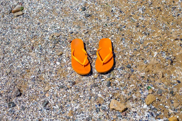 travel background with a pair of orange flip-flops in the sand