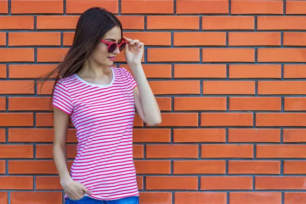 Kırmızı tuğla duvar arka plan üzerinde kırmızı güneş gözlüğü güzel genç kız portresi