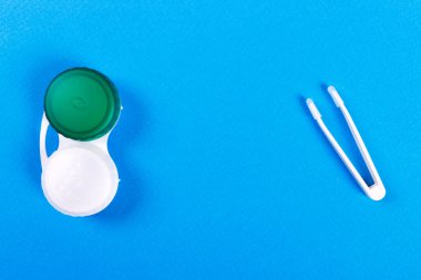 Cımbız ile Kontakt lens ve mavi arka plan üzerinde plastik konteyner
