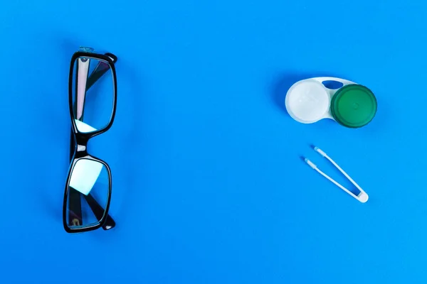 Glasögon, kontaktlinser i behållare och pincett på blå bakgrund — Stockfoto