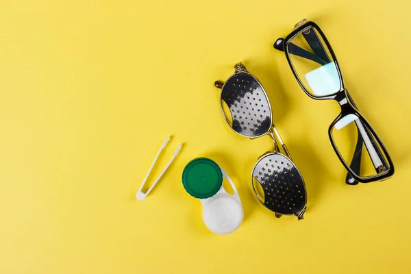 Un conjunto de accesorios para la vista. Lentes estenopeicas, lentes con contenedor y gafas para la vista. Par de gafas estenopeicas médicas con reflejos. Concepto médico. Vista superior — Foto de Stock