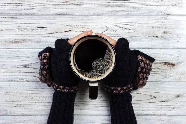 Руки женщины в варежках, держа чашку кофе на деревянном фоне — стоковое фото