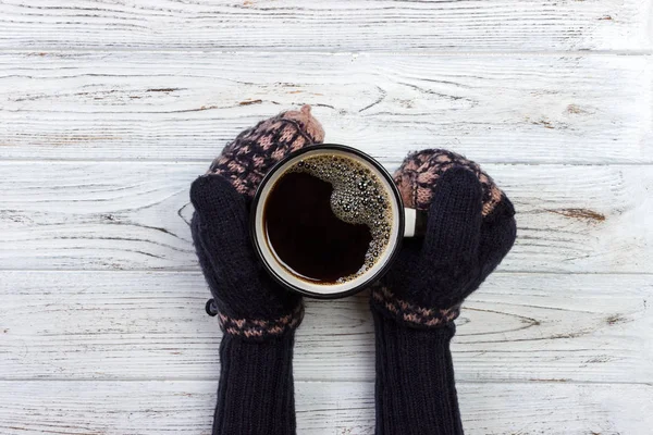 Female hands in mittens holding a cup of coffee on wooden background — Stock Photo, Image