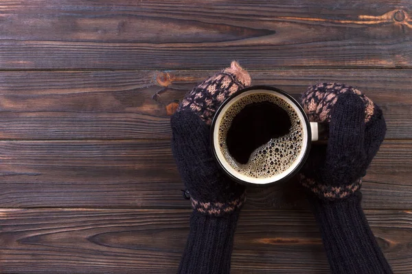 Female hands in mittens holding a cup of coffee on wooden background — Stock Photo, Image