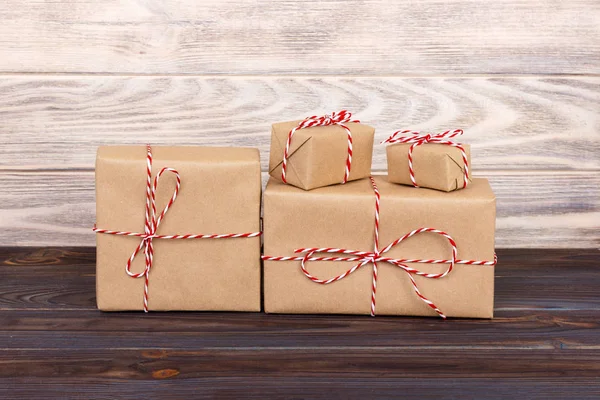 Alcune scatole regalo di Natale pacchi di carta avvolto con carta kraft e legato con rosso bianco panettiere spago in un tavolo di legno scuro. Scatole regalo di Natale — Foto Stock