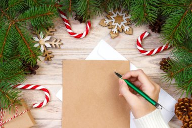 Kız el ahşap arka plan üzerinde süslemeleri ile Kraft kağıt üzerinde Noel mektup yazma