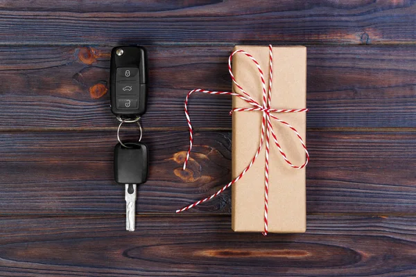 Car key near paper box with red ribbon bow on wooden table background. Christmas or Valentine\'s Day gift or present abstract concept