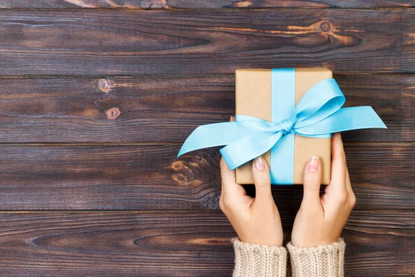 Vrouw handen geven verpakt Valentijn of andere vakantie met de hand gemaakt in papier met blauw lint. Aanwezig doos, decoratie van geschenk op witte houten tafel, bovenaanzicht met kopieerruimte — Stockfoto