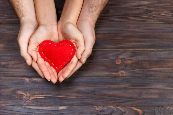 Amor, concepto familiar. Primer plano de las manos de hombre y mujer que sostienen el corazón de goma roja juntos — Foto de Stock