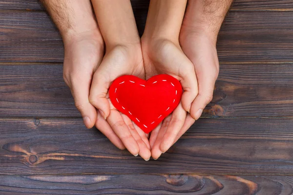 Corazón rojo en manos de hombre y mujer, sobre fondo de madera — Foto de Stock