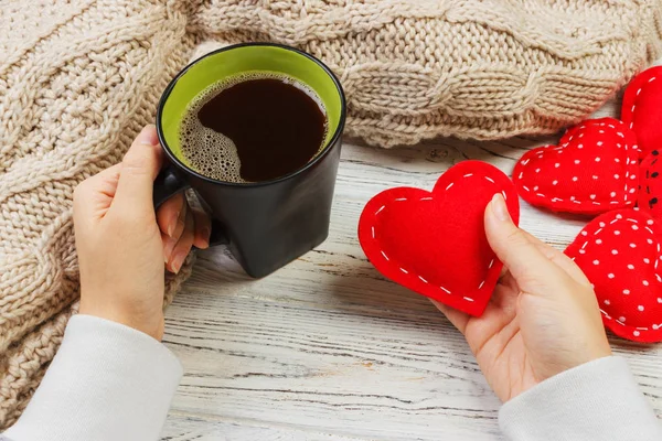 Above view of female hand holding hot cup of coffee with red heart on wood table. Photo in vintage color image style