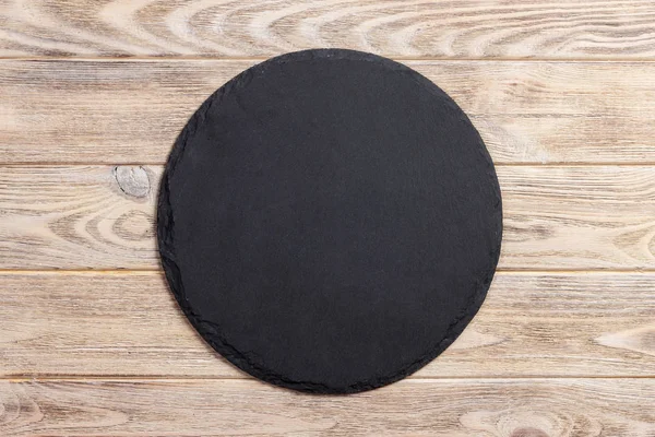 Round natural slate board. Dark gray slate stand on wooden background. Natural restaurant utensil — Stock Photo, Image