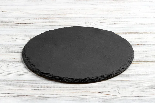 Round natural slate board. Dark gray slate stand on wooden background. Natural restaurant utensil