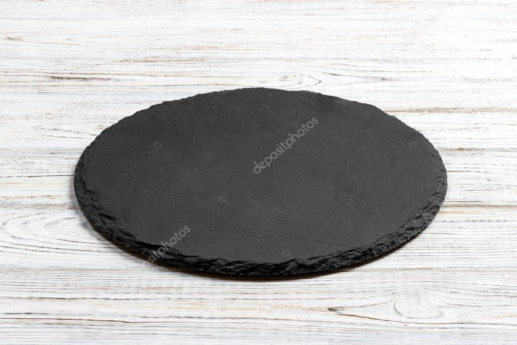 Round natural slate board. Dark gray slate stand on wooden background. Natural restaurant utensil