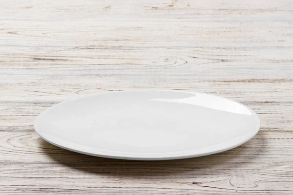 Weißer runder Teller auf weißem Holztischhintergrund. perspektivische Sicht — Stockfoto