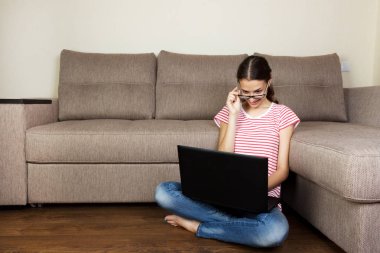 Sevimli öğrenci kız belgili tanımlık laptop. Işık daire yerde oturan genç kadın