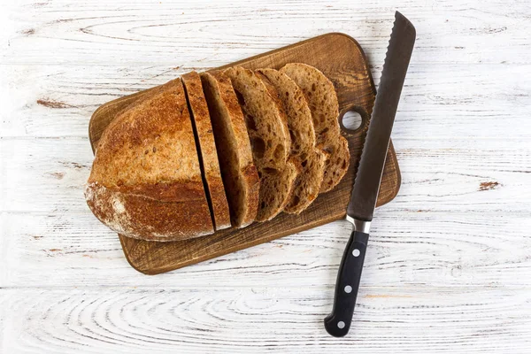 Wooden cutting board with sliced white bread and knife on wooden table