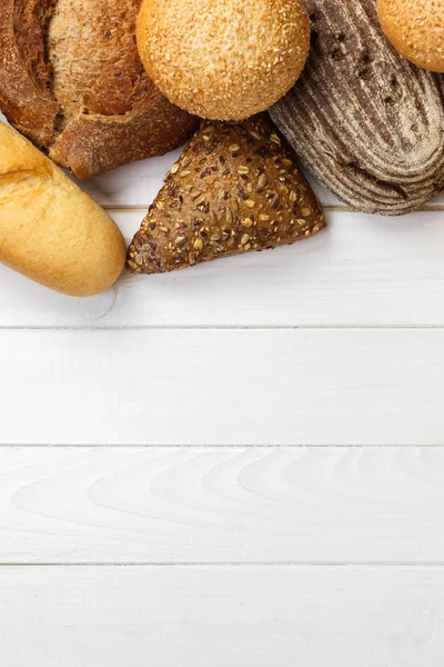 Surtido de pan fresco sobre un fondo de madera blanca. vista superior con espacio de copia — Foto de Stock