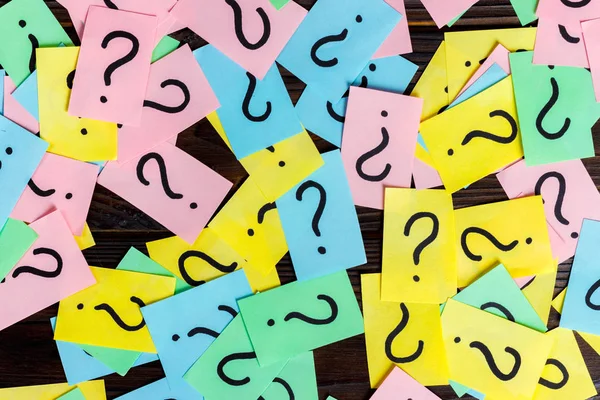 Túl sok kérdés a fa háttér. Egy halom színes papírt kérdőjelekkel. felülnézet — Stock Fotó