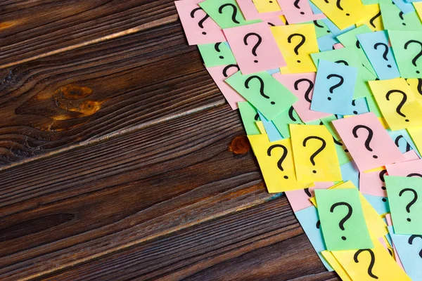 Nur viele Fragezeichen auf farbigen Papieren auf Holzgrund — Stockfoto