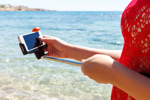 Girl in red swimsuit adjusts camera on selfie stick in the sea — Stock Photo, Image