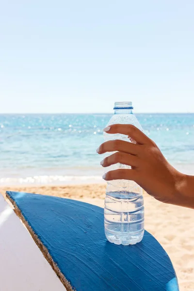 Weibliche Hand hält eine Flasche Wasser am Strand, Meereshintergrund — Stockfoto