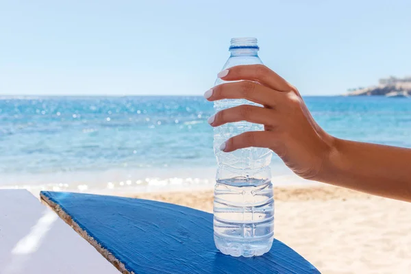 Mãos femininas segurando uma garrafa de água na praia — Fotografia de Stock
