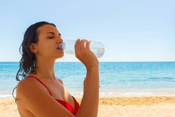 Schöne brünette Mädchen in roten Badeanzug Wasser trinken an einem Urlaubstag — Stockfoto