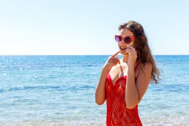 Mutlu gülümseyen kız sahilde mobil akıllı telefon kullanarak. Kız deniz cep telefonuyla konuşurken