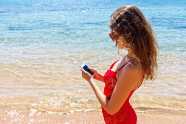 Bir akıllı telefon kullanarak mayo giyen sunbather kız. yaz tatili sahilde