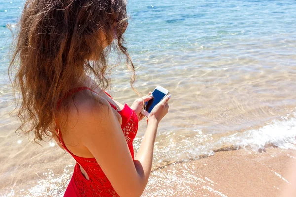 Acercamiento mujer mensajes de texto en un teléfono inteligente en la playa. mar en el fondo —  Fotos de Stock